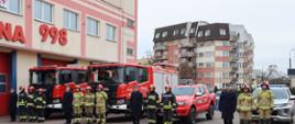 Strażacy na tle nowo przekazanych aut pożarniczych. Dwa ciężkie samochody ratowniczo-gaśnicze na podwoziu SCANIA z napędem 4x2 i dwa lekkie samochody ratowniczo-rozpoznawcze, jeden to: Ford Ranger o napędzie 4×4 i drugi to Mitsubishi L200 o napędzie 4x4. 