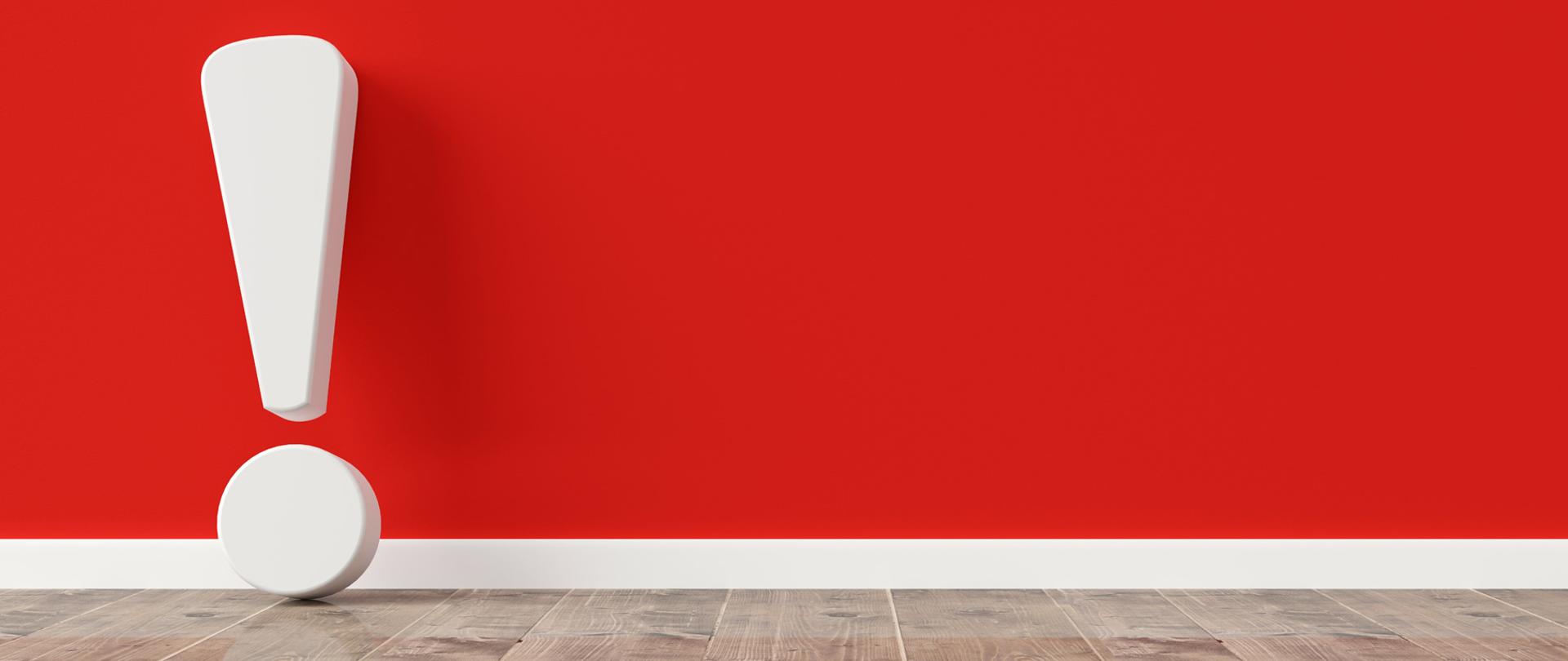Biały wykrzyknik oparty o czerwoną ścianę.