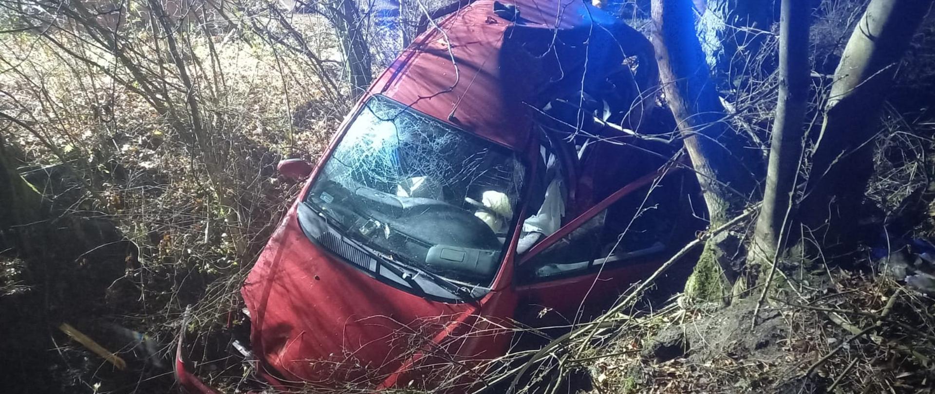 Widać samochód w głębokim rowie przy drzewie, jest ciemno