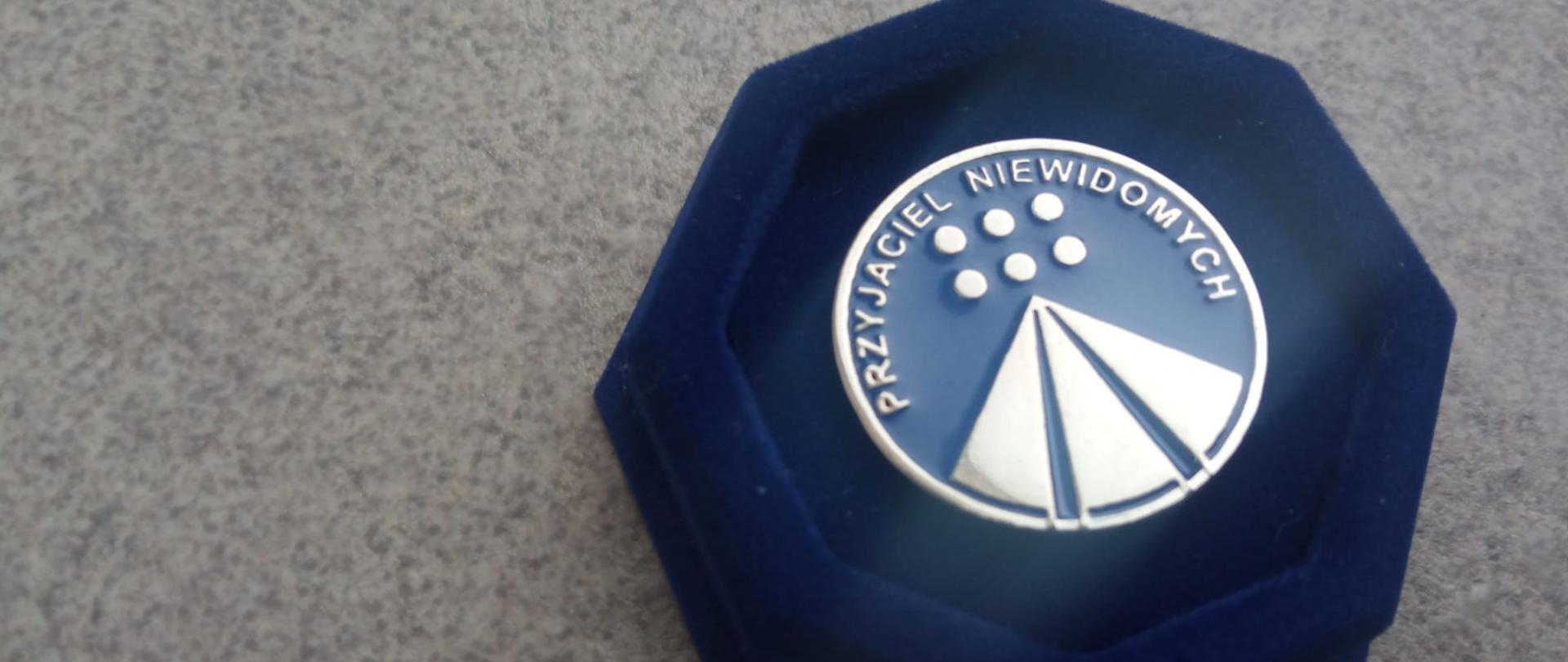 W niebieskim futerale leży znaczek z napisem przyjaciel niewidomych.