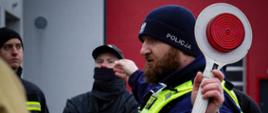 Policjant prowadzi instruktaż dotyczący zabezpieczenia miejsca zdarzenia podczas szkolenia OSP.