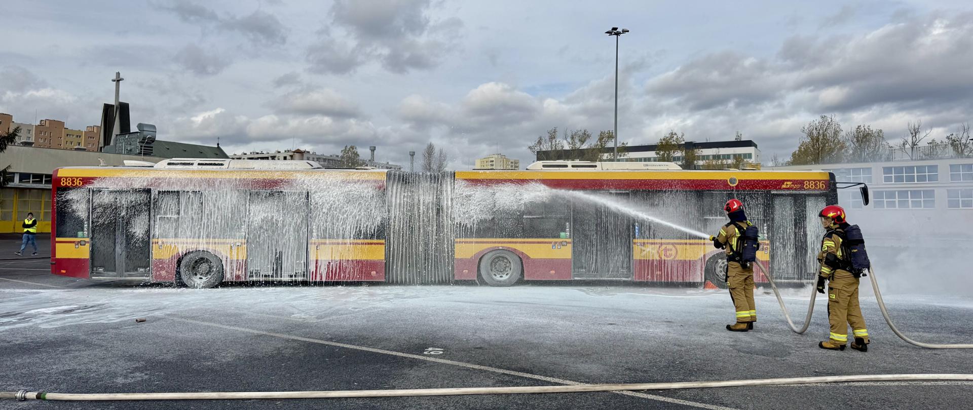 Strażacy w aparatach ODO podają prąd piany na autobus