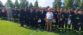 Zdjęcie przedstawia grupę ludzi strażaków PSP i OSP oraz osób cywilnych, stojących w kilku rzędach na trawniku.