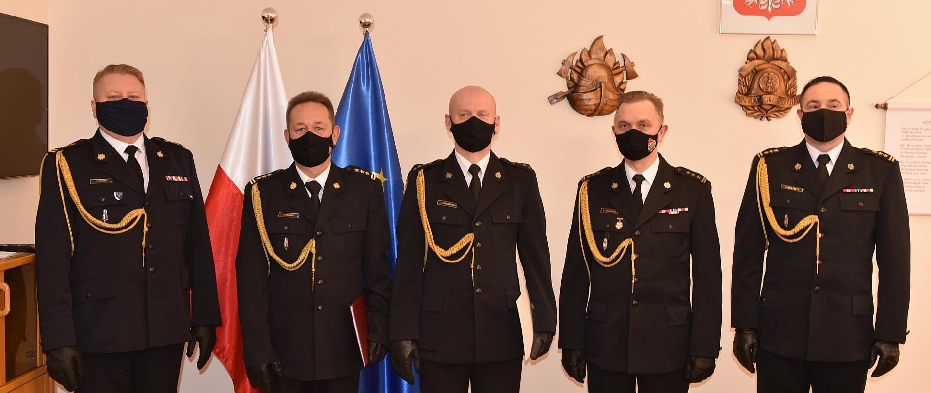 Na zdjęciu znajduje się pięciu strażaków w mundurach wyjściowych, w tle flagi polski i unii europejskiej