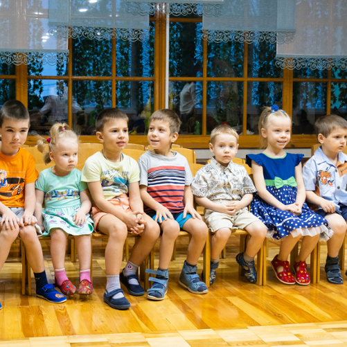 Dzieci w krótkich spodenkach siedzą na krzesłach.