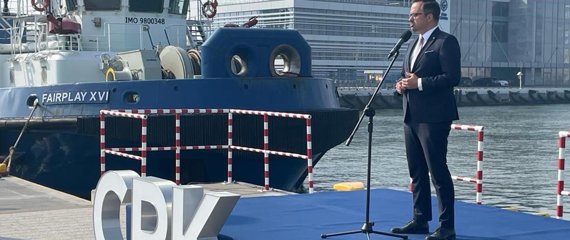 Wiceminister Marcin Horała stoi na podeście i mówi do mikrofonu.