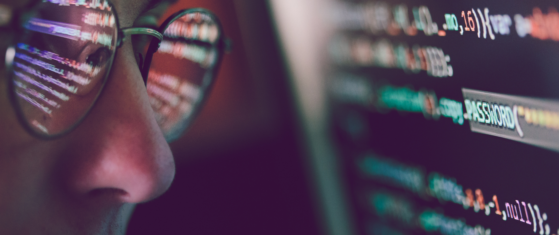 Zbliżenie na twarz mężczyzny w okularach (w domyśle ekspert cyberbezpieczeństwa) przyglądającego się ekranowi, na którym wyświetla się ciąg znaków, w tym słowo password (hasło).