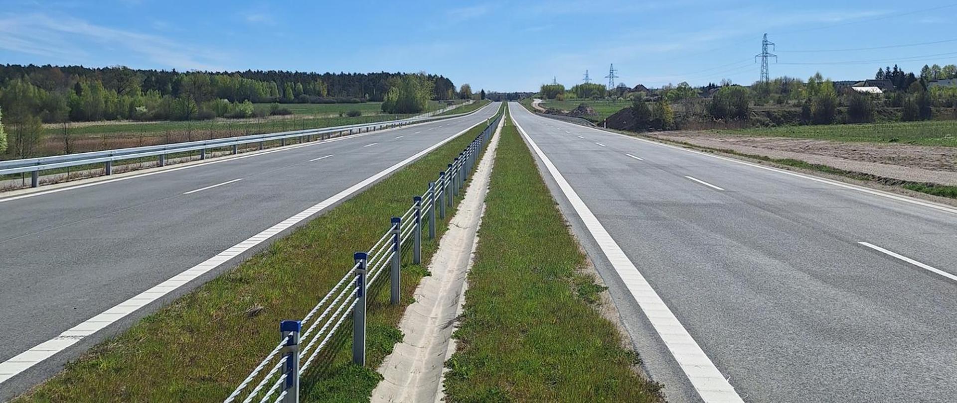 DK42 obwodnica Wąchocka - dwujezdniowa droga asfaltowa, po obu stronach zieleń, w oddali pojedyncze zabudowania