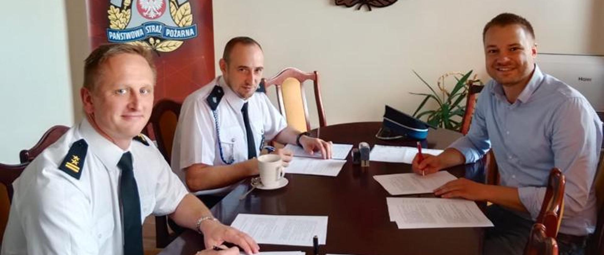 Na zdjęciu znajdują się Komendant powiatowy KP PSP w Strzelcach Op., Prezes OSP Olszowa oraz Burmistrz Ujazdu na tle logo PSP podczas podpisywania dokumentów