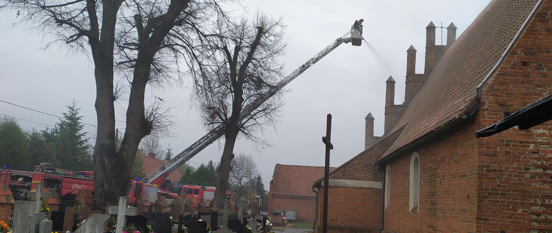 Strażacy z kosza drabiny mechanicznej podają prąd wody na pozorowany pożar kościoła
