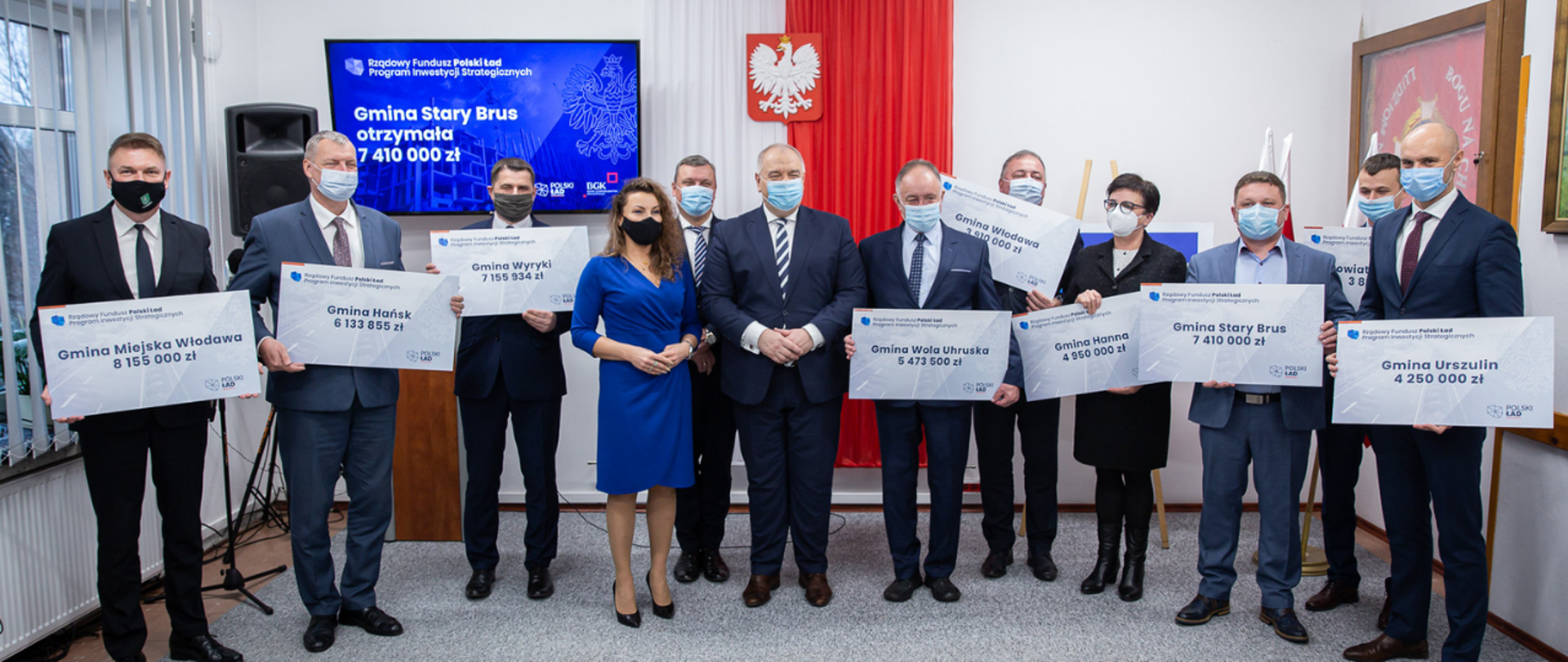 Zdjęcie grupowe dwunastu osób. Na środku wicepremier Jacek Sasin. Wokół niego włodarze z powiatu włodawskiego trzymający symboliczne czeki