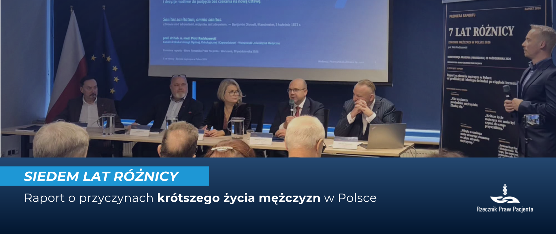 Prelegenci siedzą za stołem, nad nimi jest ekran z prezentacją, Widać uczestników konferencji od tyłu. 