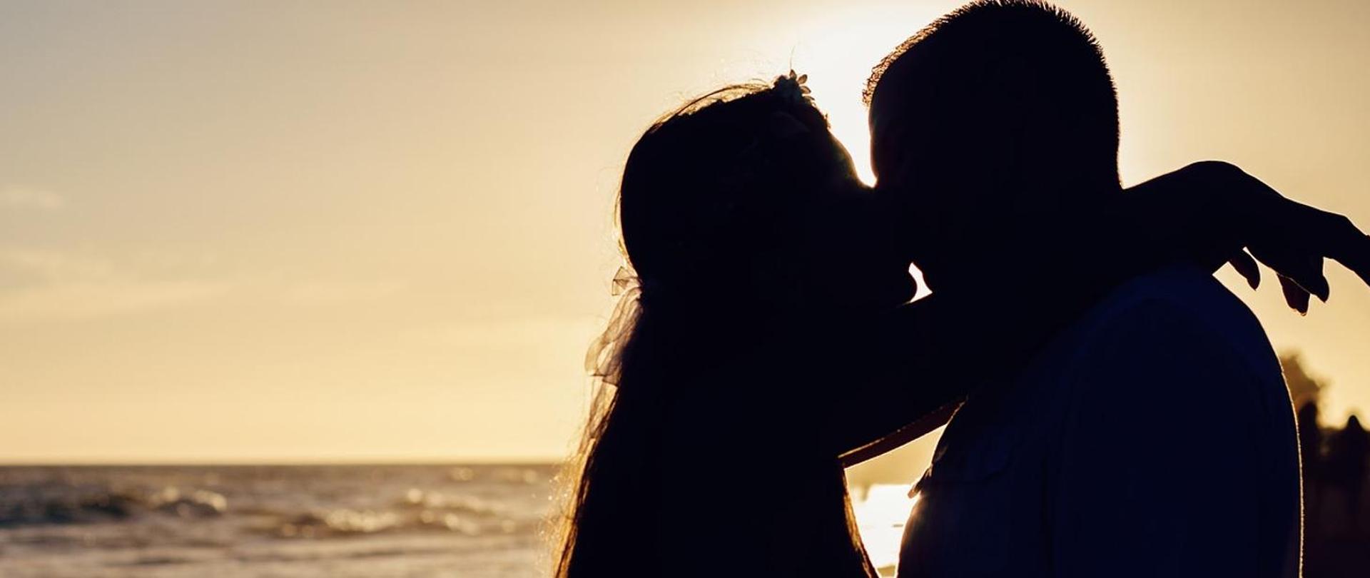 na tle zachodzącego słońca dwoje całujących się ludzi