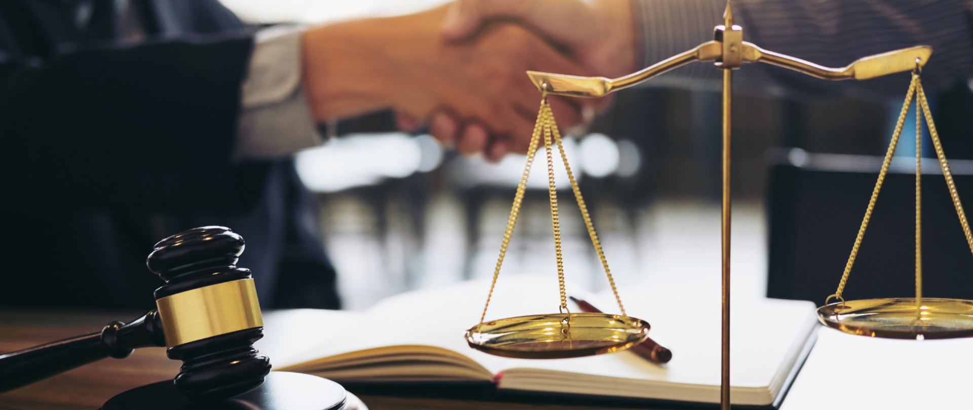 dwie osoby podają sobie dłonie, jest waga i młoteczek symbolizujące wymiar sprawiedliwości 