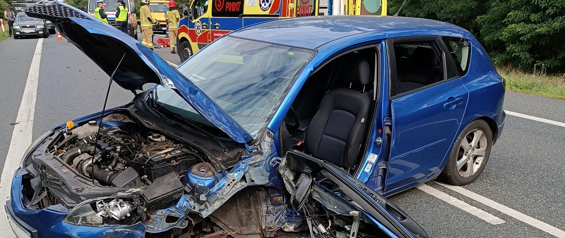 Samochód osobowy po wypadku, w tle ambulans, strażacy oraz policjanci