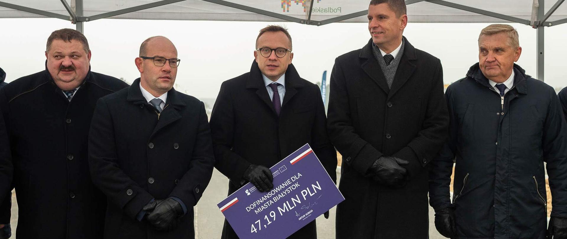 uczestnicy uroczystości stoją, wiceminister Artur Soboń trzyma czek z napisem 47,19 mln zł