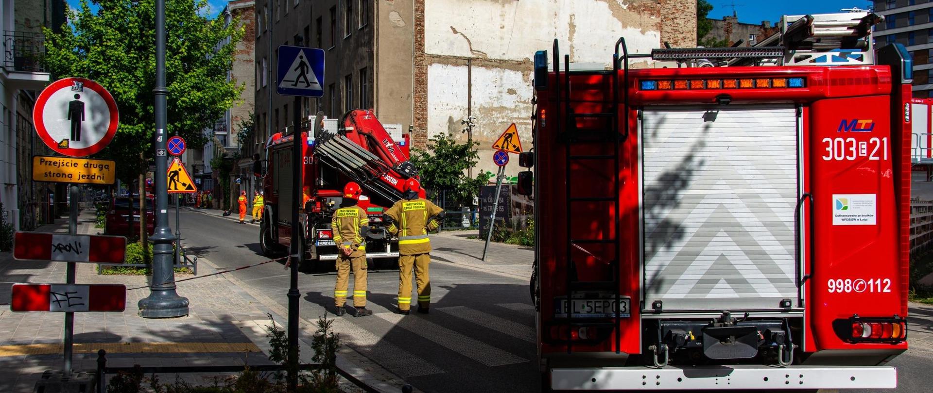 Samochody pożarnicze, w tle kamienica w której doszło do katastrofy budowlanej. Pomiędzy pojazdami dwóch strażaków