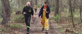 Na zdjęciu widać czterech strażaków, którzy przemieszczają się leśną ścieżką, a w rękach trzymają urządzenia GPS.