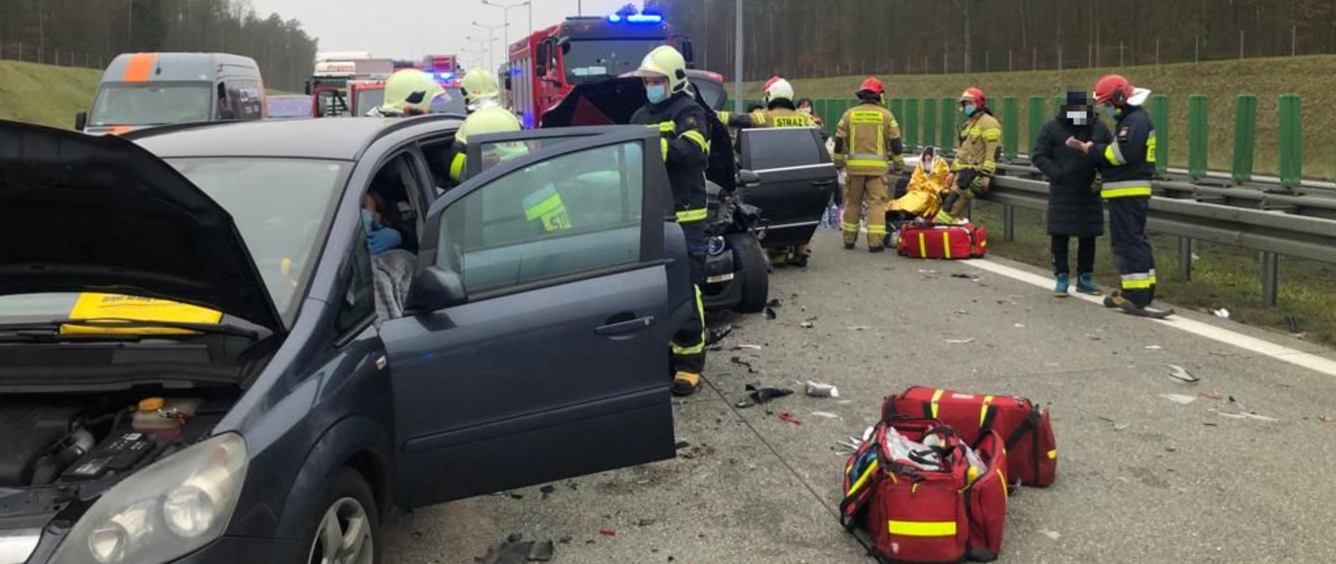 Dzień, uszkodzone pojazdy, strażacy udzielający pomocy medycznej.