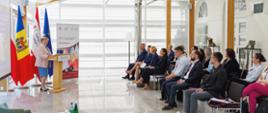 Conference room full of people with women speaking. Behind her are Polish, Molfovan and EU flags