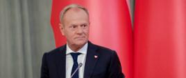 Premier Donald Tusk podczas posiedzenia Rady Gabinetowej 27.08.2025 r. W tle biało-czerwone flagi.