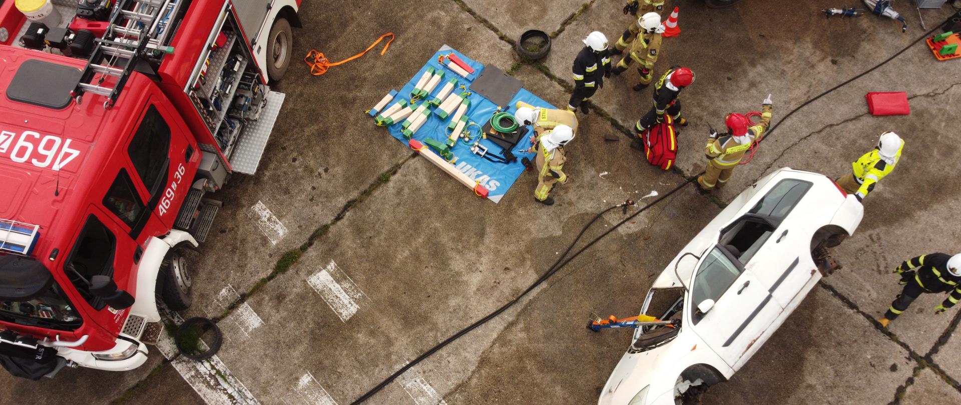 Zdjęcie przedstawia działania strażaków podczas ćwiczeń Śniatowo 2021. Widać samochód na boku strażaków oraz wozy i sprzęt strażacki.