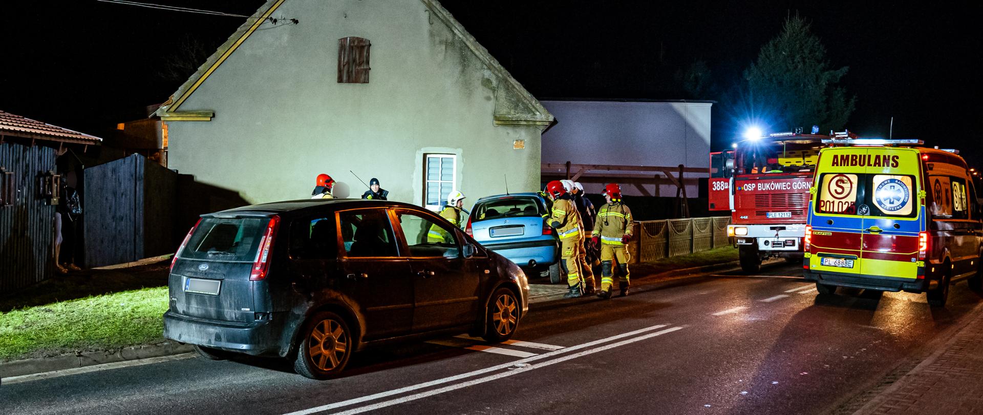 Samochód osobowy uderzył w budynek obok pracujący strażacy i samochody ratownicze.