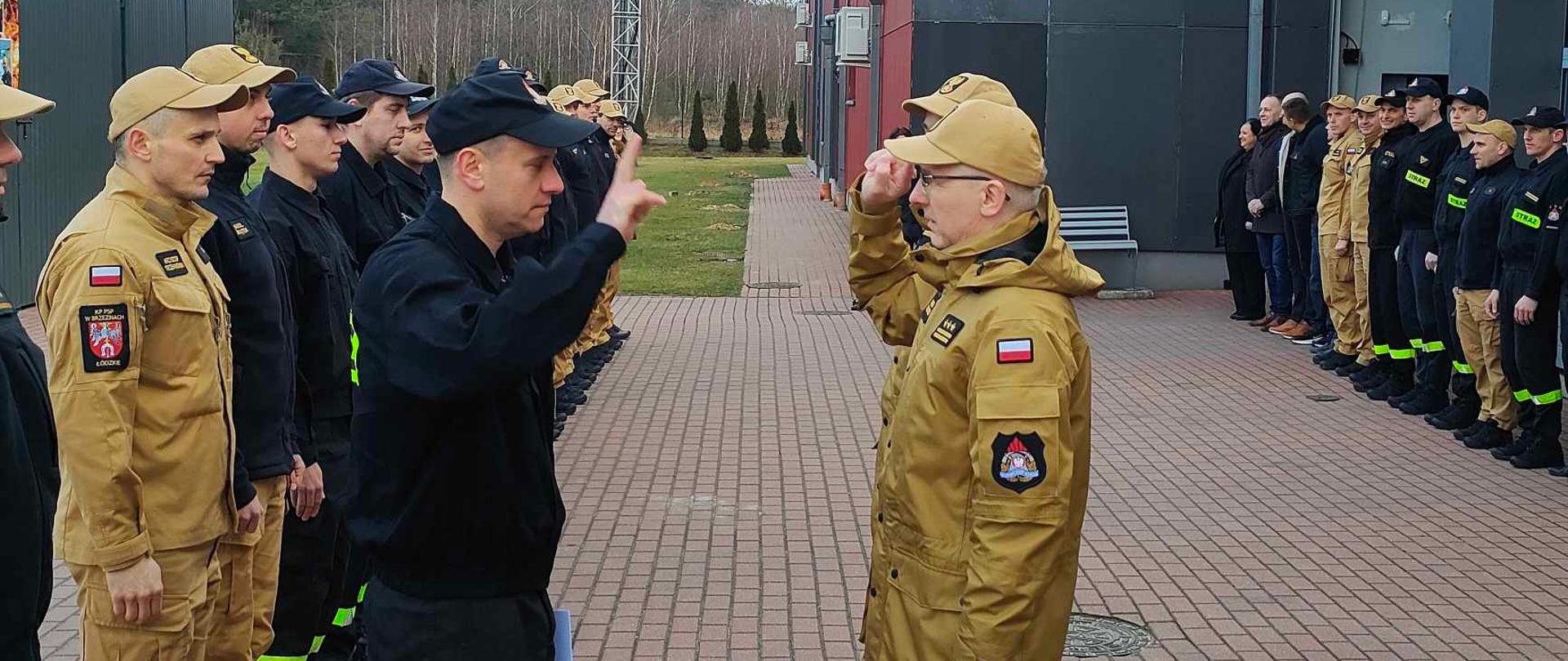 Przejście na zaopatrzenie emerytalne starszego ogniomistrza Krzysztofa Sobieszkody. Komendant Powiatowy Państwowej Straży Pożarnej w Brzezinach starszy brygadier Mariusz Kaczmarski wręcza decyzję zwalniającą funkcjonariusza ze służby. Podczas wręczania decyzji asystuje zastępca Komendanta Powiatowego Państwowej Straży Pożarnej w Brzezinach młodszy brygadier Jakub Brzózka. Sytuacja ma miejsce podczas uroczystej zbiórki na placu komendy, strażacy stoją w dwóch szeregach na przeciw siebie.