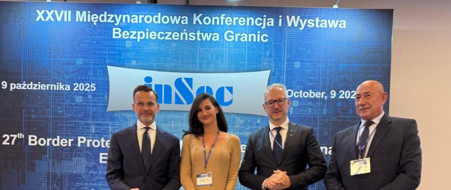 Cztery osoby stoją na tle niebieskiej ścianki, trzech mężczyzn i jedna kobieta 