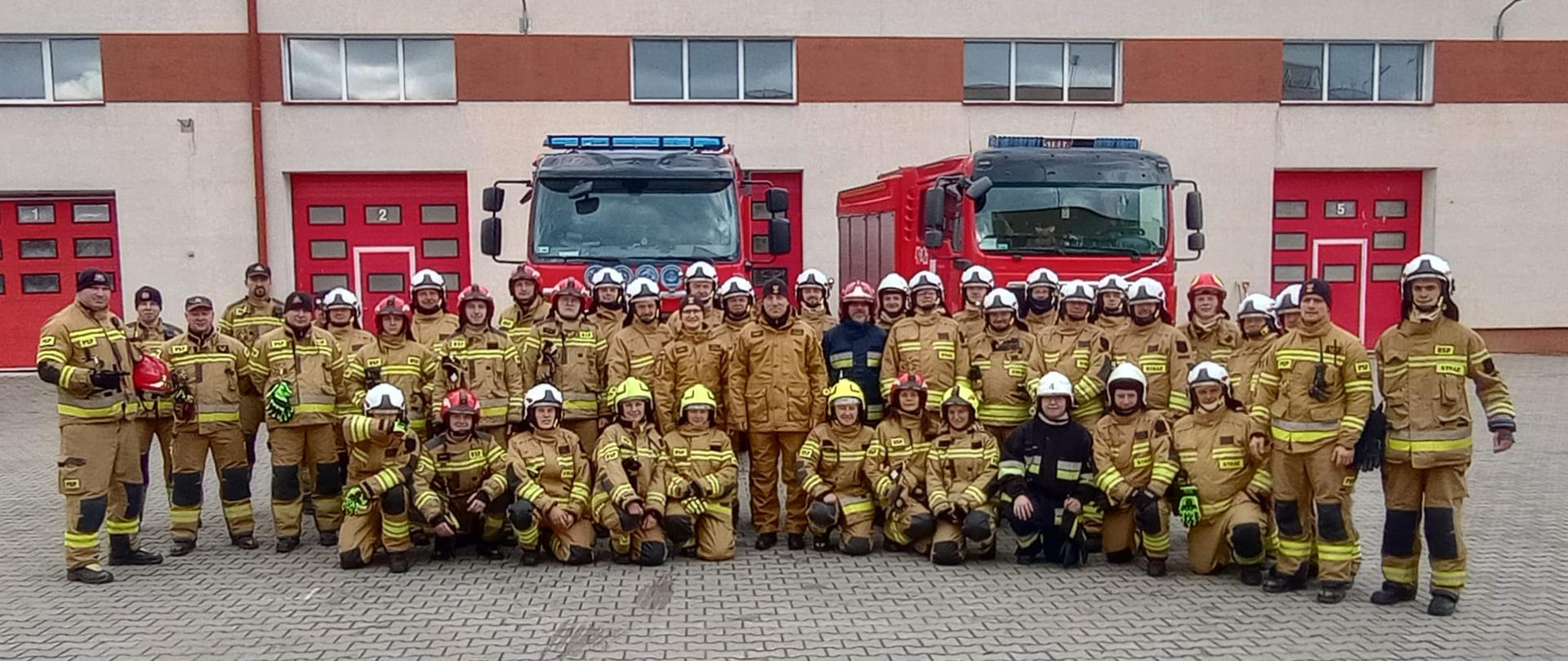 Zdjęcie grupowe strażaków biorących udział w szkoleniu. Za nimi dwa samochody pożarnicze.