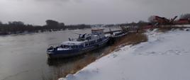 Fragment koryta rzeki Wisły z zaśnieżonym brzegiem, na której z prawej strony przy zacumowana barka.