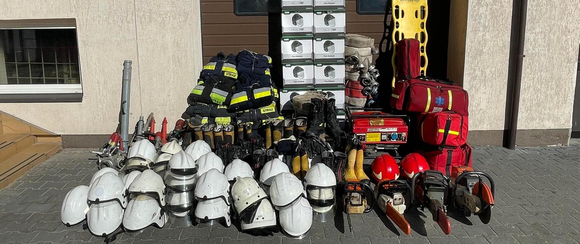 Zdjęcie przedstawia zgromadzony pod jedną z bram garaży na terenie Komendy Powiatowej Państwowej Straży Pożarnej w Zambrowie sprzęt ratowniczy przeznaczony dla strażaków z Ukrainy, w tym m. in. hełmy, torby PSP R1, piły, prądownice.