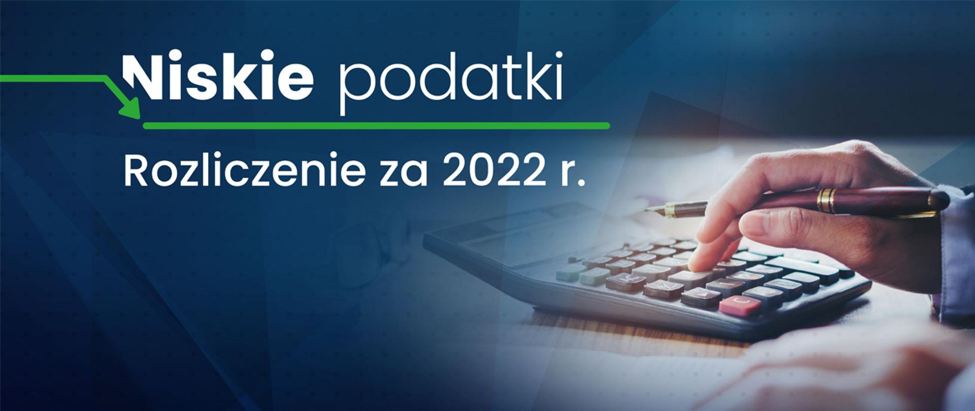Dłoń z piórem, kalkulator, napis Niskie podatki rozliczenie za 2022 r.