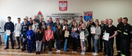 Zdjęcie grupowe na świetlicy KP PSP. Na zdjęciu uczestnicy konkursy czyli młodzież szkolna oraz organizatorzy. Dzieci trzymają w rękach nagrody oraz dyplomy. 