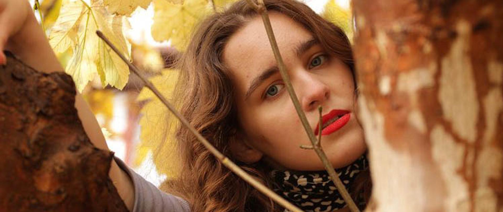 Portret dziewczyny z pniami drzew i jesiennymi liśćmi w tle