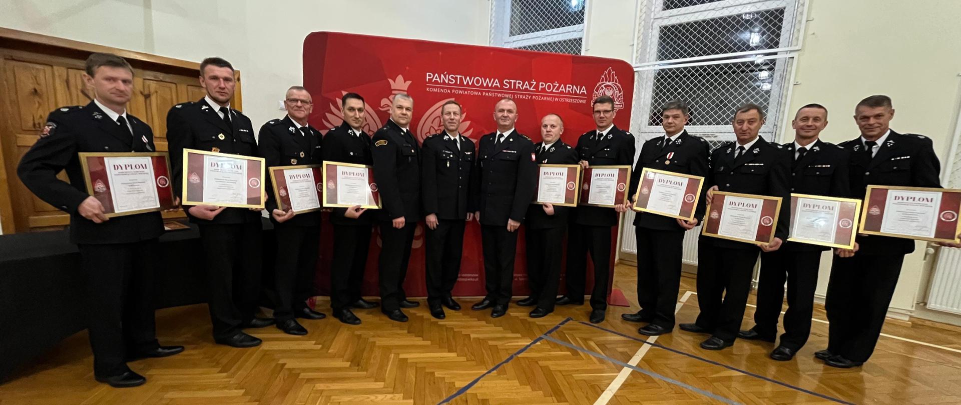 Druhowie z pamiątkowymi dyplomami pozują do zdjęcia, w tle banner. Zdjęcie wykonane w sali gimnastycznej.