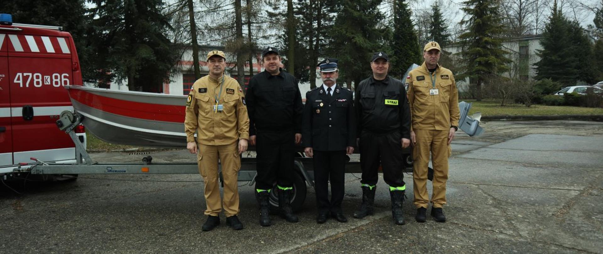 Komendant Centralnej Szkoły PSP, w towarzystwie trzech druhów OSP oraz oficera CS PSP na tle przekazywanej łodzi ratowniczej