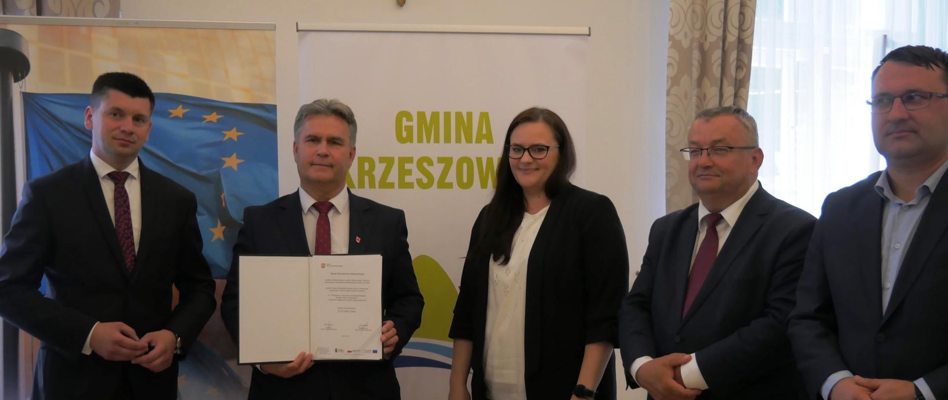 Pięć osób - czterech mężczyzn, a pomiędzy nimi kobieta (minister Małgorzata Jarosińska-Jedynak) stoją przed ścianką promocyjną Gmina Krzeszowice