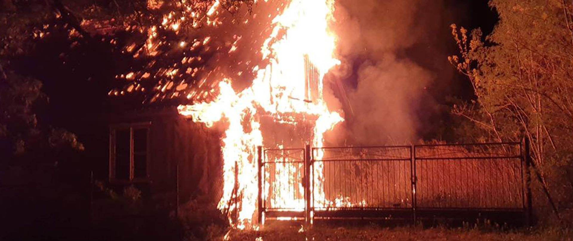 Na zdjęciu widoczny jest płonący drewniany budynek. Ogniem objęta jest ściana szczytowa oraz poddasze.