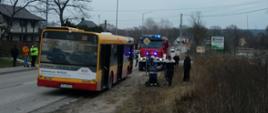 Zdjęcie przedstawia autobus Solaris z otwartymi drzwiami - nie widać na nim żadnych uszkodzeń. Przed autobusem widać kilku pasażerów. W tle znajduje się samochód Straży Pożarnej