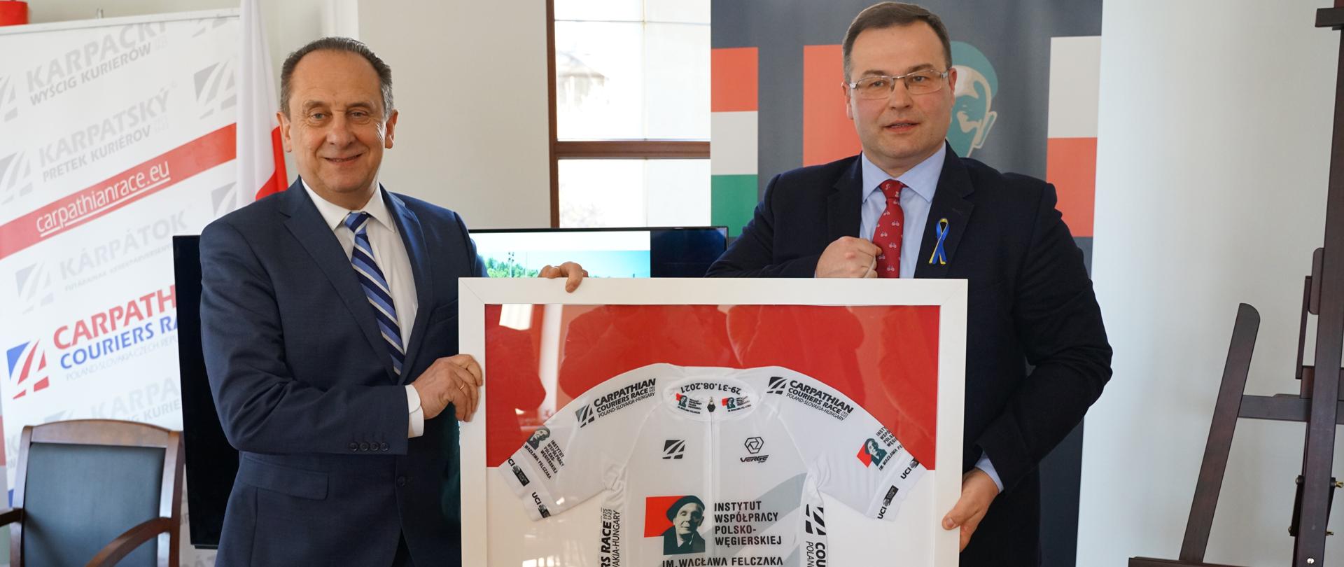 Wiceminister Gut-Mostowy gościem konferencji zapowiadającej 39. edycję Karpackiego Wyścigu Kurierów pamięci Wacława Felczaka. Na zdjęciu minister Gut-Mostowy oraz Tomasz Wójcik, dyrektor wyścigu, trzymają pamiątkową koszulkę kolarską z wizerunkiem Wacława Felczaka