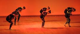 Zdjęcie tancerek na scenie w pozycji skłonu. Zdjęcie w pomarańczowym oświetleniu.