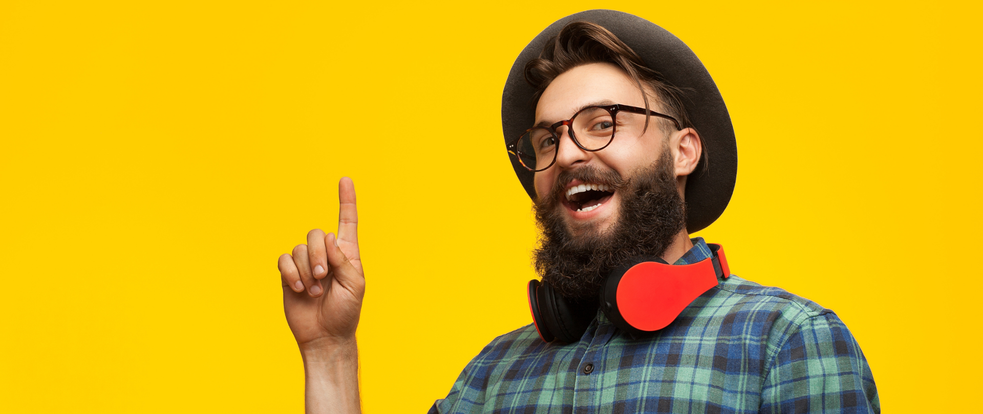 Młody mężczyzna z brodą, w okularach i kapeluszu na żółtym tle. Jego wyraz twarzy i uniesiony palec prawej dłoni wskazują, że właśnie wpadł na dobry pomysł.