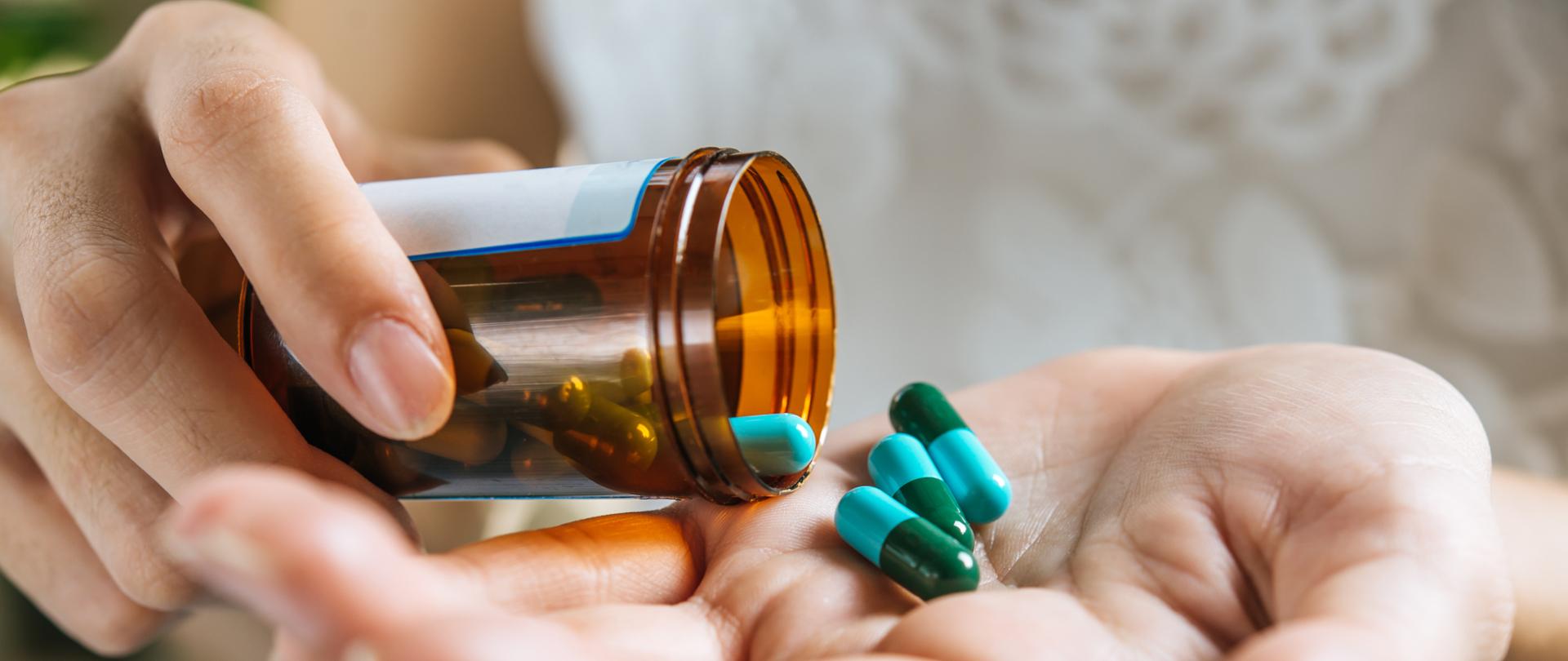 Zdjęcie przedstawia dłonie kobiety, która wysypuje leki, antybiotyki z opakowania na rękę. 