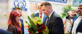 Minister Czarnek wręcza kobiecie bukiet czerwonych kwiatów, za nimi ściana z napisem Zespół Szkól Akademickich.