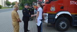 Plac przed komendą powiatową PSP. P.o. komendanta wita się z załogą komendy. 