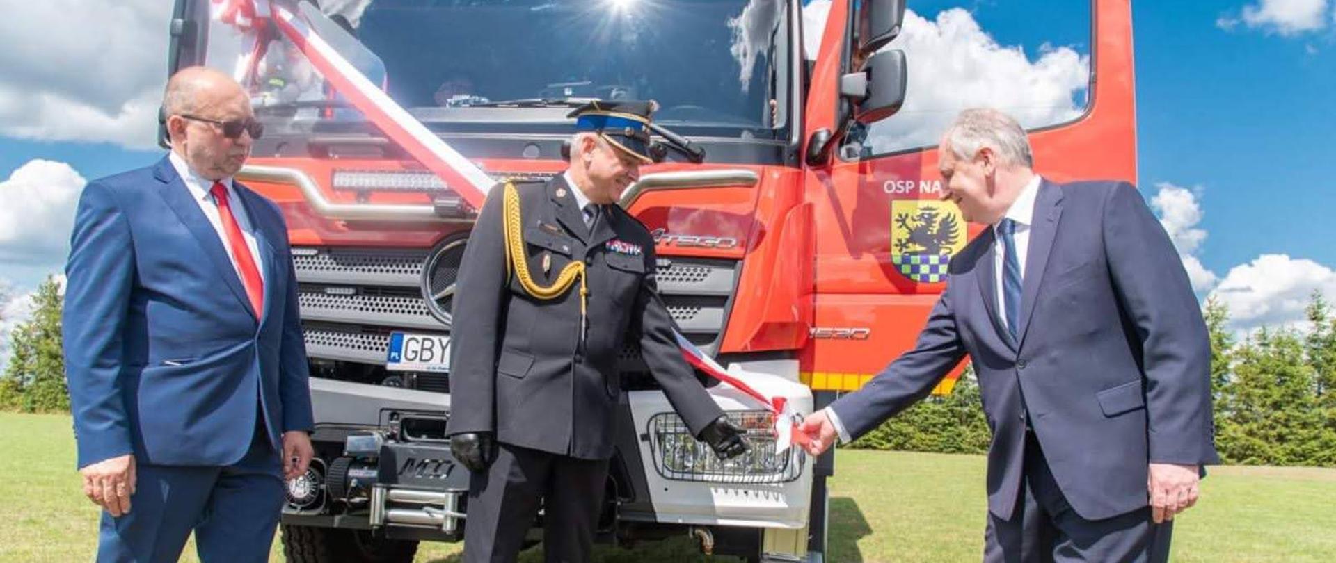 Wojewoda pomorski, pomorski komendant wojewódzki Państwowej Straży Pożarnej oraz wójt gminy Parchowo symbolicznie zrywają szarfę z nowego samochodu gaśniczego.