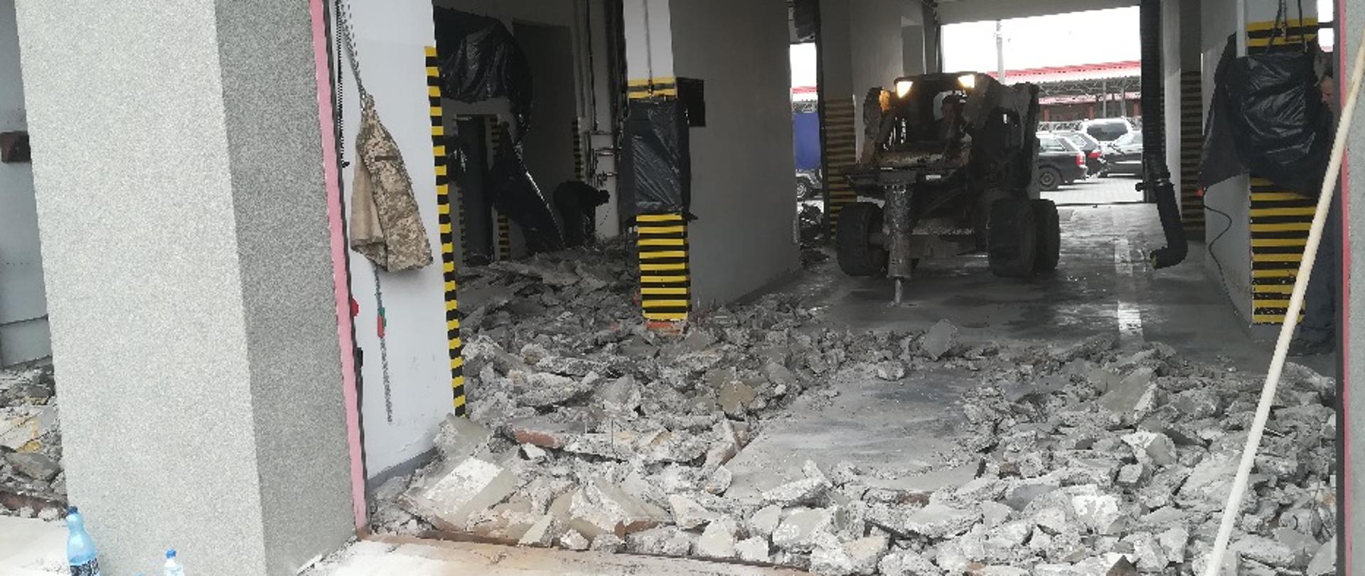 Fotografia przedstawiająca prace rozbiórkowe starej posadzki garażowej na którym widać maszynę do skuwania betonu krusząca starą posadzkę garażową.