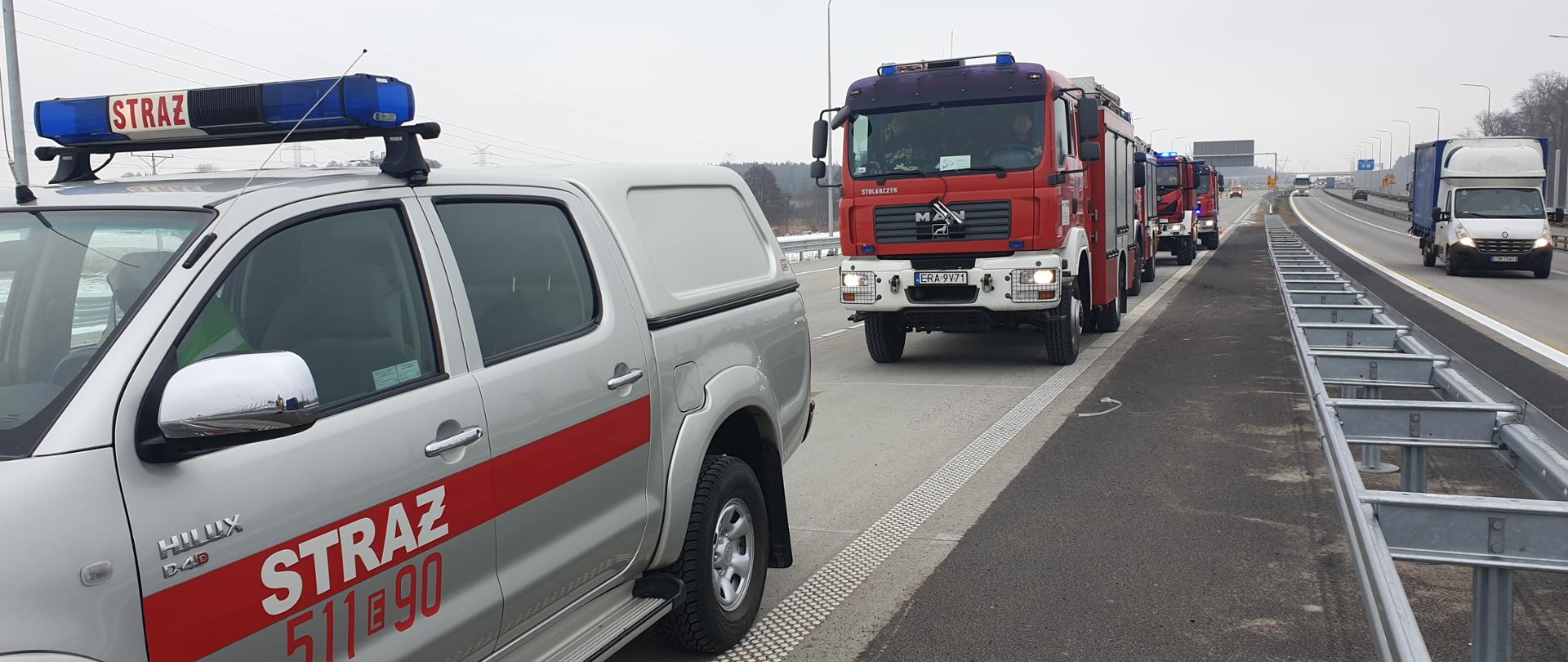 Pięć pojazdów pożarniczych na nowo budowanej autostradzie, obok przejazdu awaryjnego.
