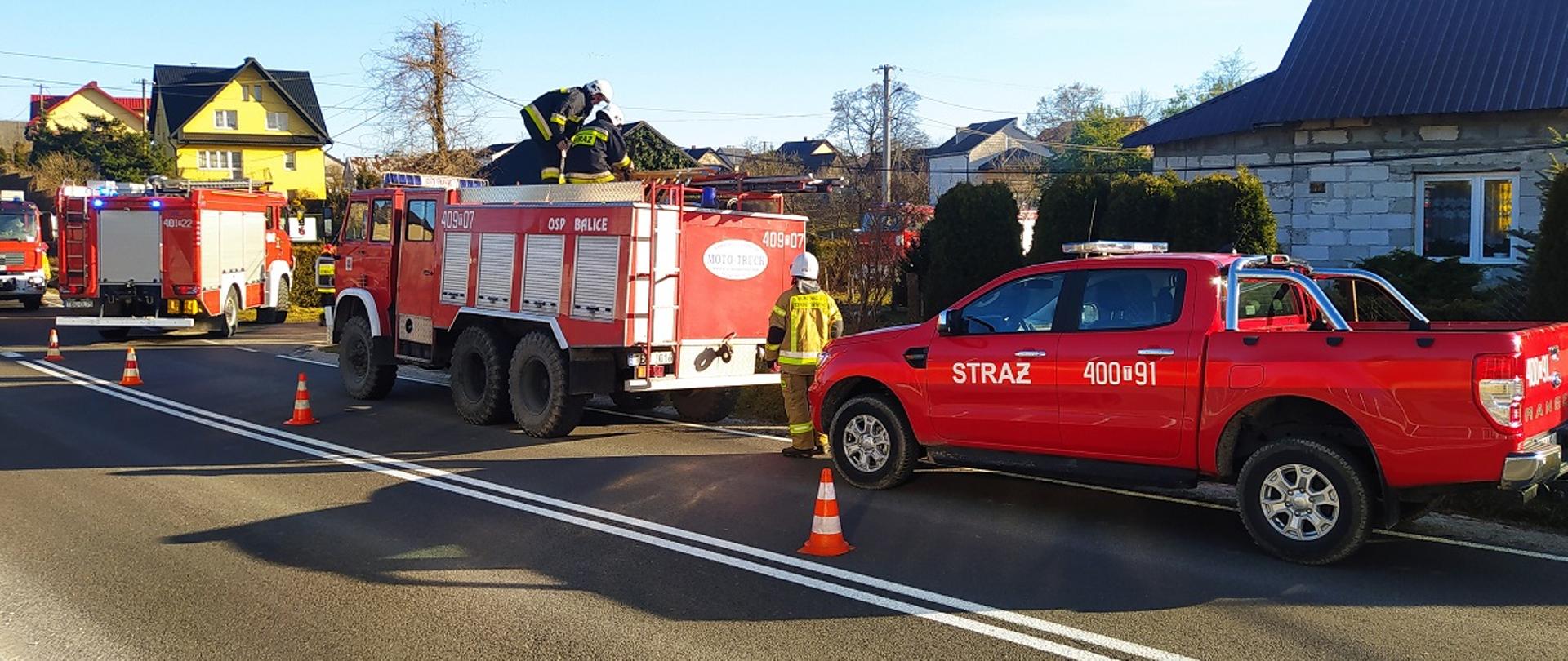 Zdjęcie przedstawia samochody pożarnicze ustawione na drodze przed budynkiem w którym wybuchł pożar
